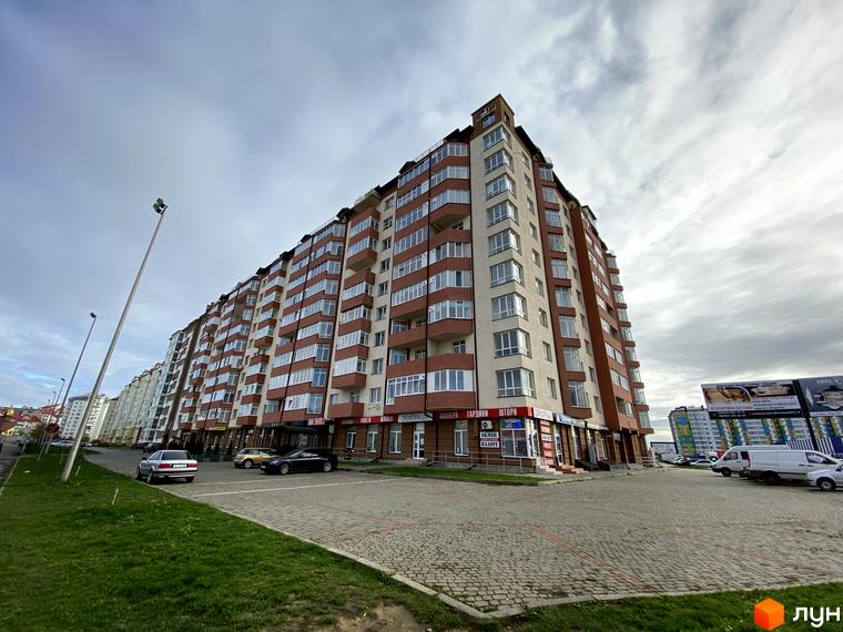 Зображення багатоповерхового будинку на вул. Стуса / вул. Миколайчука. Вигляд фасаду з вікнами та балконами, прибудинкова територія з паркінгом.