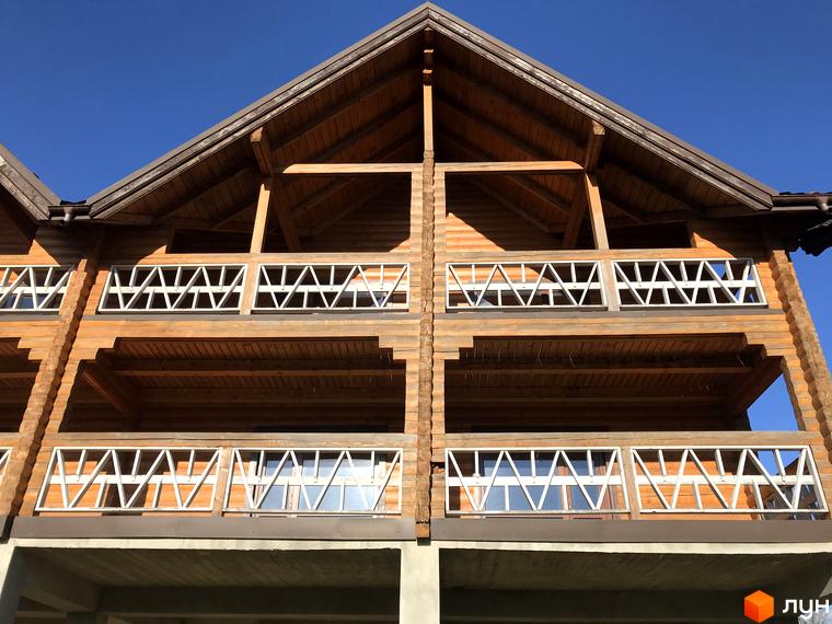 Котеджне містечко КМ Семидвір. Двоповерховий дерев'яний будинок з балконами та вікнами на тлі блакитного неба.