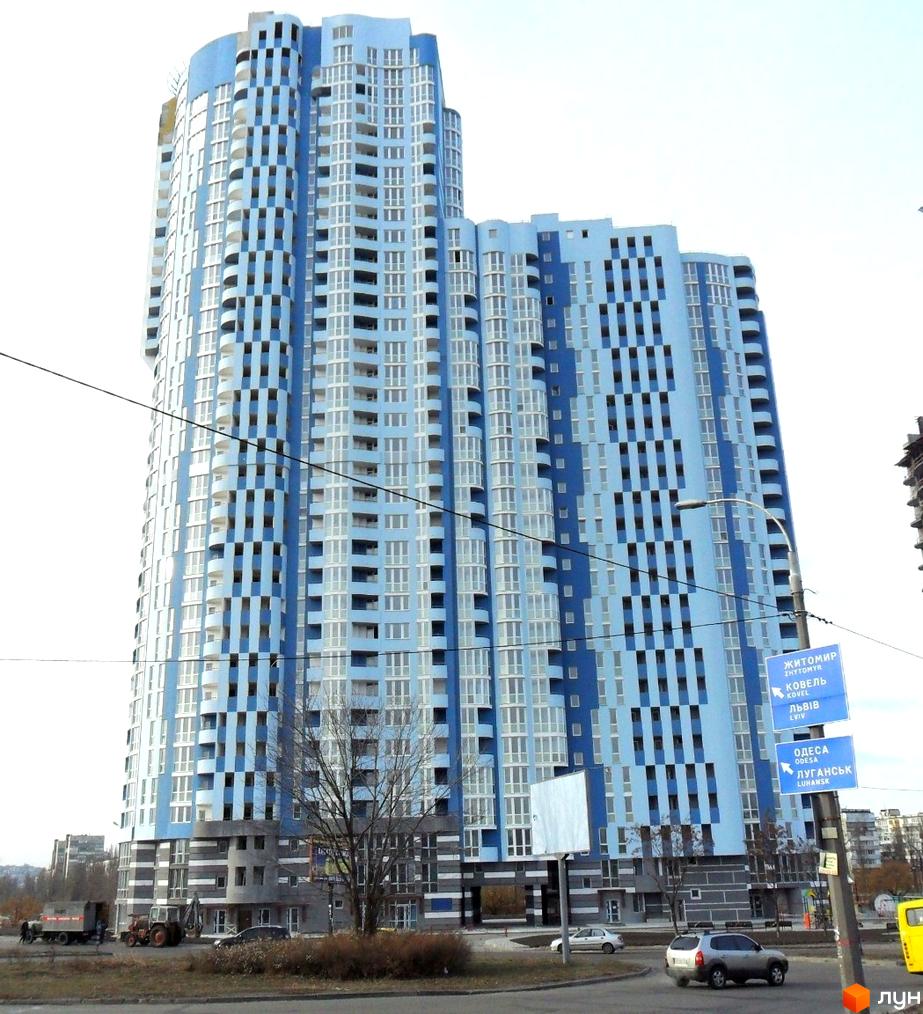 Житловий комплекс Київська Венеція – висотна новобудова блакитного кольору з численними вікнами та балконами. Навколо комплексу розташовані дороги та дерева.