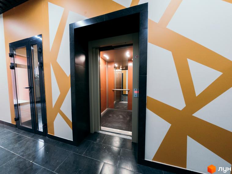 Зображення холу з дверима та ліфтом у житловому комплексі на вул. Транспортна, 10. Дизайн стін з геометричними візерунками.