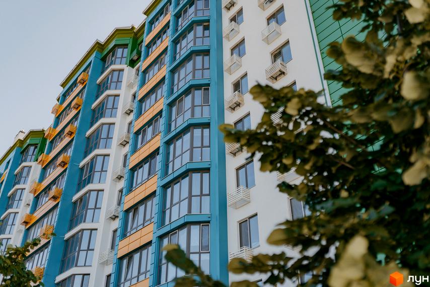 Житловий комплекс Евромісто: яскрава фасадна частина багатоповерхового будинку з блакитними, жовтими та зеленими елементами. Вікна розташовані рядами, деякі з них мають виступи.