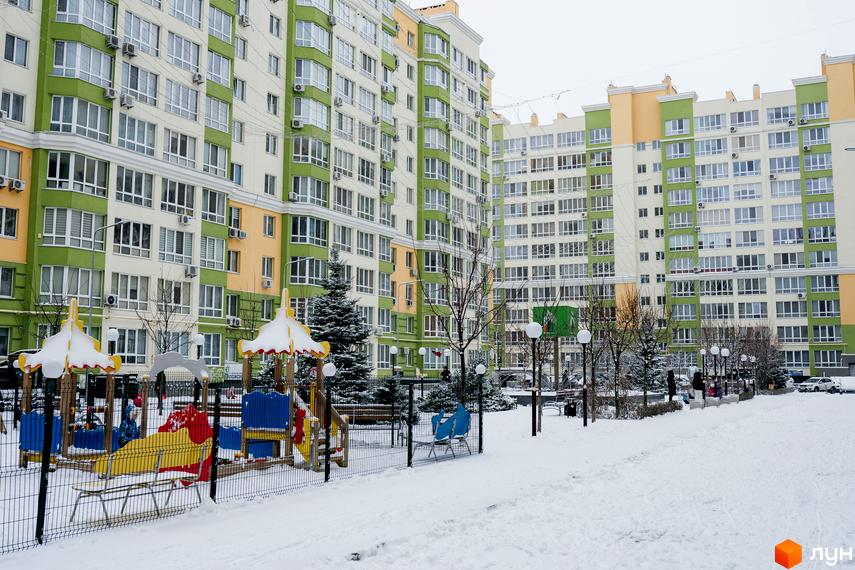 Житловий комплекс Евромісто з яскравими фасадами та дитячим майданчиком взимку. Сучасна новобудова з великою кількістю вікон та балконів, оточена засніженою територією.