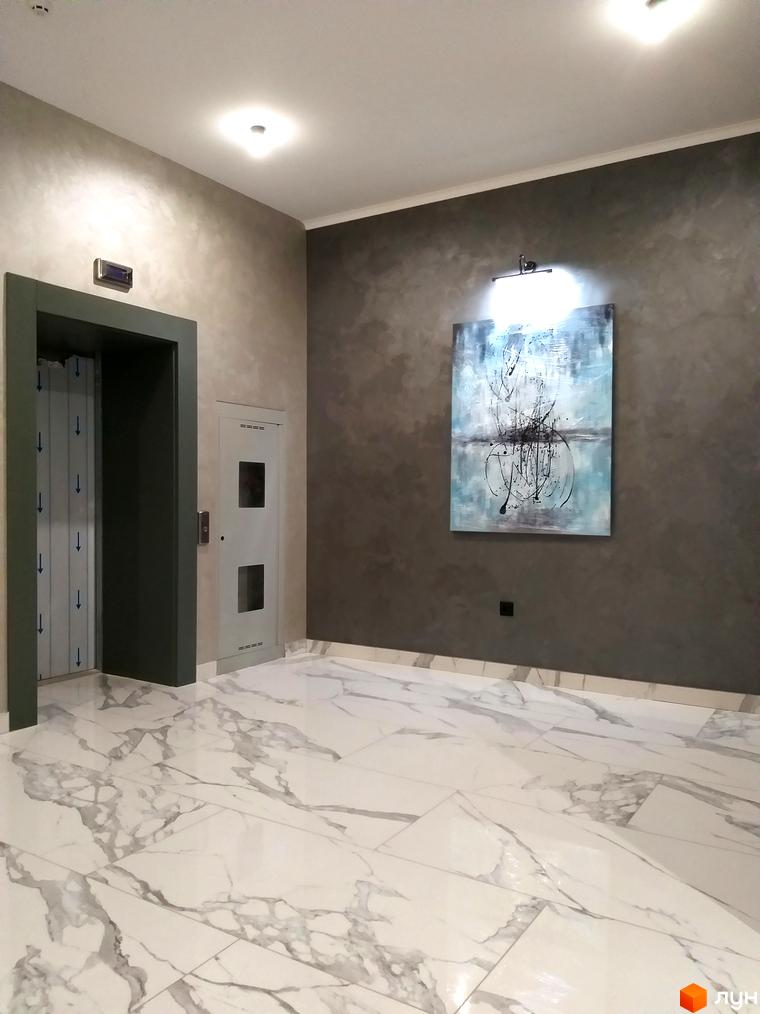 Інтер'єр холу Житлового комплексу Корфу з ліфтом та картиною на стіні. Підлога викладена плиткою під мармур.