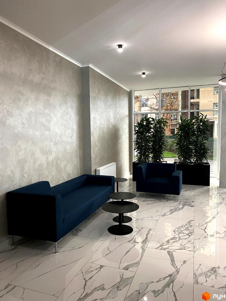 Інтер'єр зони відпочинку в Житловому комплексі Корфу. М'які меблі, журнальні столики та великі рослини у просторому холі з панорамними вікнами.