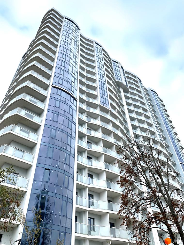 Фото фасаду багатоповерхового будинку Житлового комплексу Корфу з великими вікнами та балконами. Вигляд знизу на будівлю.