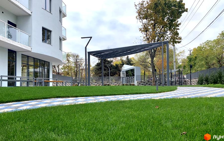 Зображення фасаду та прибудинкової території Житлового комплексу Корфу. На передньому плані газон та доріжка з плитки.