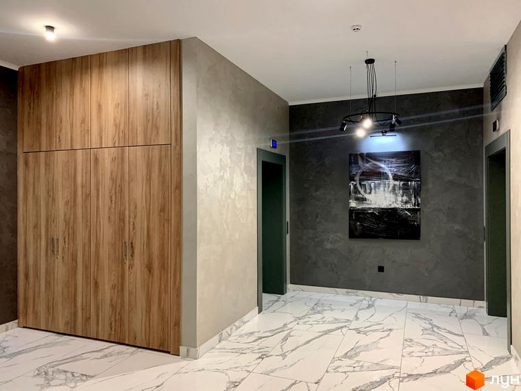 Інтер'єр вхідної групи Житлового комплексу Корфу з дерев'яними шафами та мармуровою підлогою. На стіні картина та світильник.