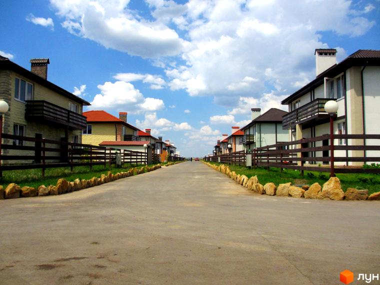 Зовнішній вигляд котеджного комплексу КМ Fresh Town з асфальтованою дорогою та зеленими територіями.