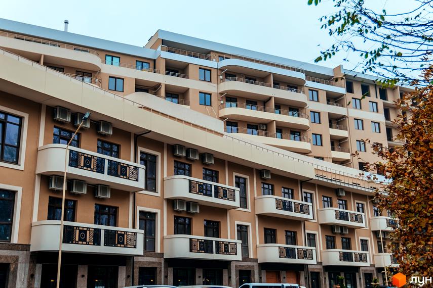 Фасад житлового комплексу DREAM CITY з балконами та кондиціонерами на коричневому фоні. Зовнішній вигляд будівлі з численними вікнами та виступаючими елементами.