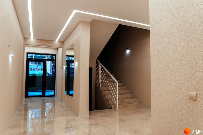 Сучасний інтер'єр холу житлового комплексу DREAM CITY з підсвіченими стелями та мармуровою підлогою. Вхідні двері та сходи ведуть на верхні поверхи.