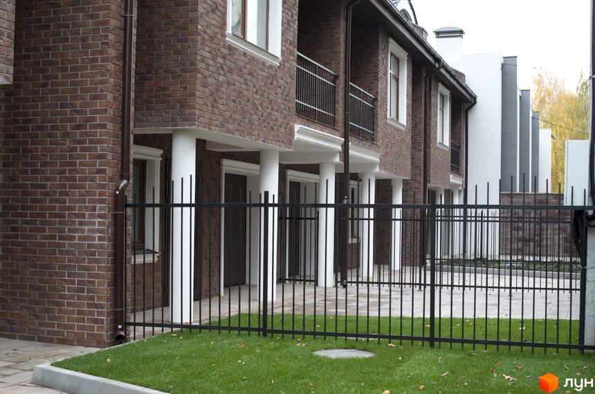 Цегляні таунхауси ЖК Протасів Residence з чорною огорожею та газоном. Фасад будинку з балконами, білими колонами та вікнами.