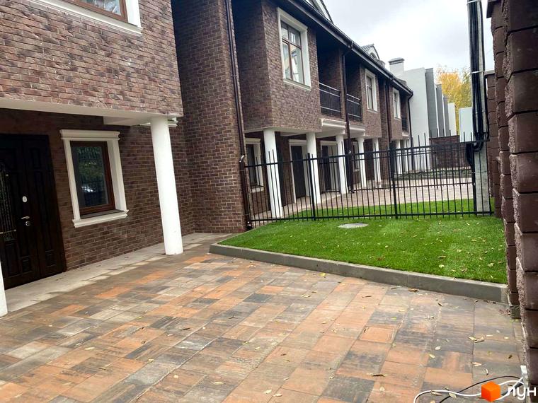 Зовнішній вигляд таунхаусів Протасів Residence з цегляними фасадами та доглянутою прибудинковою територією з газоном та бруківкою.