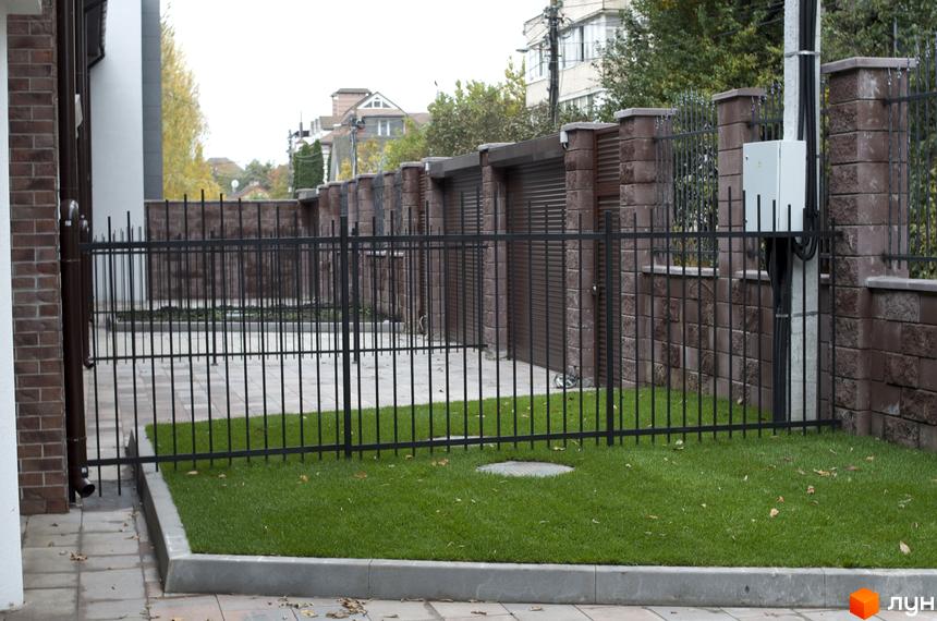 Огорожа таунхаусів Протасів Residence. Цегляний фасад будинку, газон з декоративною огорожею, бруківка.