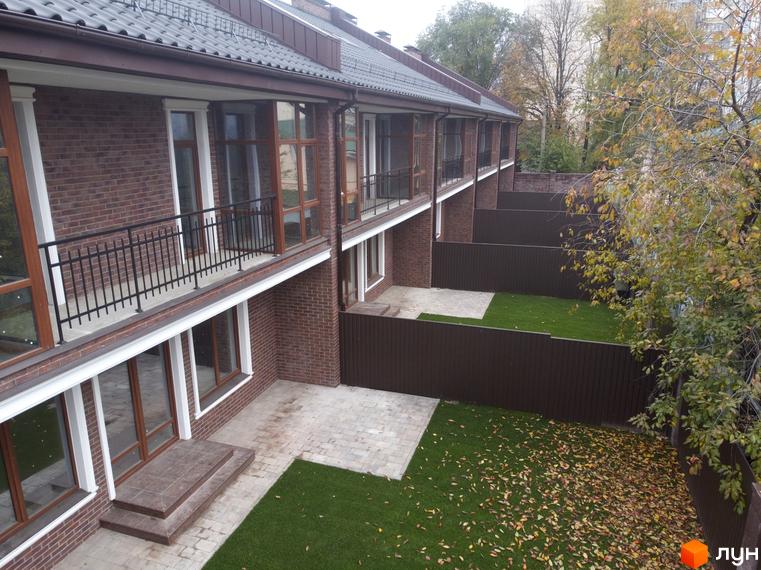 Зовнішній вигляд таунхаусів Протасів Residence з цегляними фасадами, балконами та доглянутою прибудинковою територією з газонами та парканами.