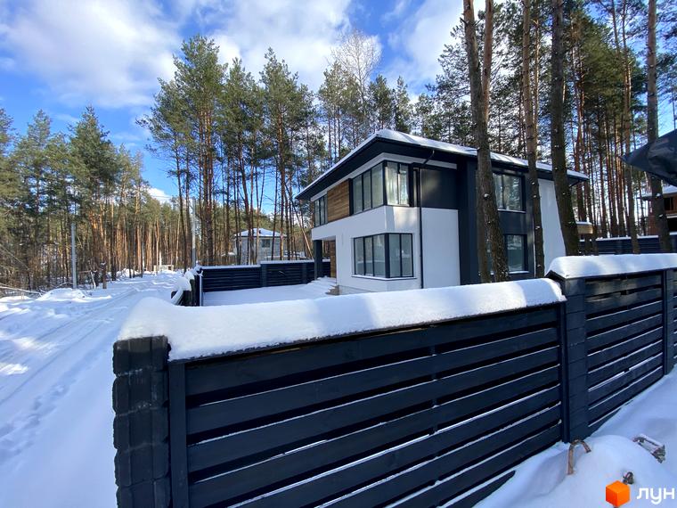 Котеджне містечко Квітка Полонини. Двоповерховий будинок з великими вікнами, чорним дахом та парканом. Навколо сніг та дерева.