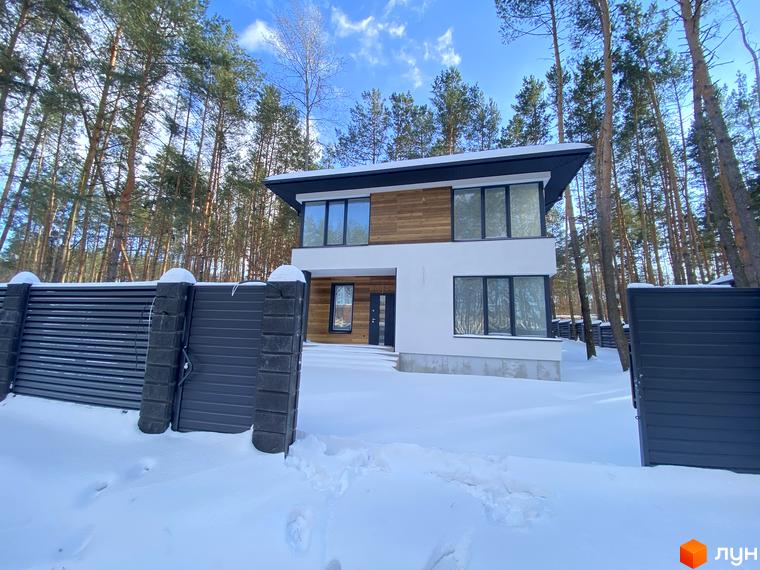 Двоповерховий будинок з панорамними вікнами та дерев'яним оздобленням на фасаді. Котеджне містечко Квітка Полонини серед засніжених дерев.