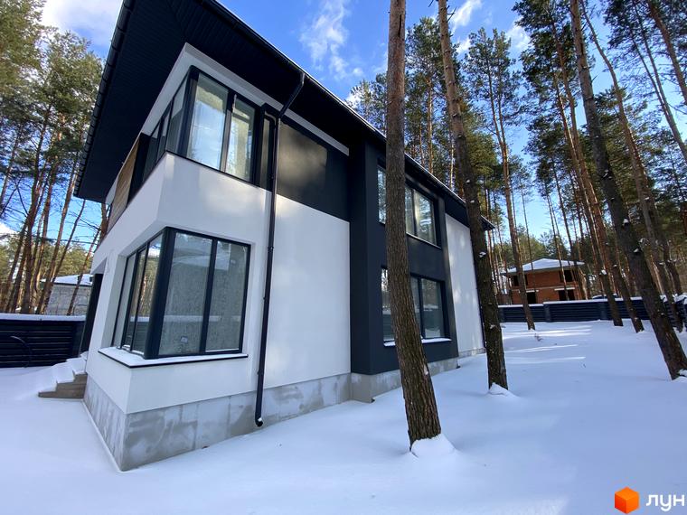 Котеджне містечко Квітка Полонини. Двоповерховий будинок з великими вікнами на тлі засніженої території та дерев.