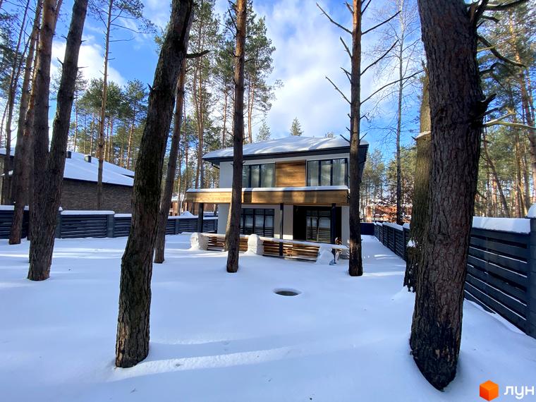 Двоповерховий будинок з панорамними вікнами в Котеджному містечку Квітка Полонини, вкритий снігом. На території багато дерев та огородження.
