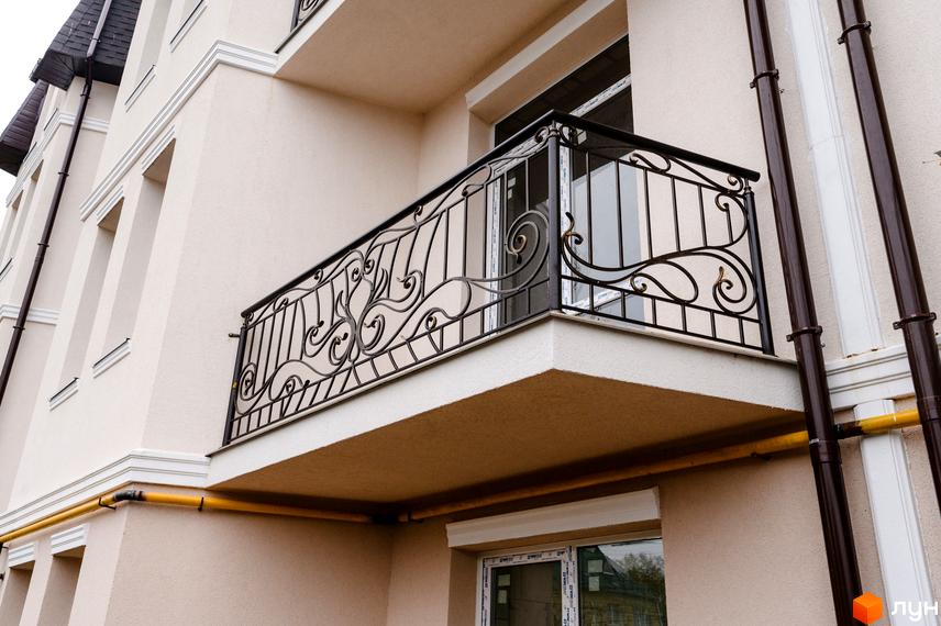 Фасад будинку Житлового комплексу по вул. Академіка Вернадського (Тульська), 21а з кованим балконом та трубами. Бежевий колір стін, вікна та жовті труби.