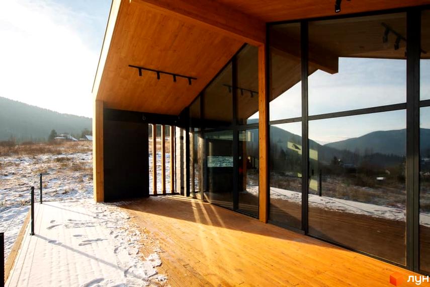 Дерев'яний будинок з панорамними вікнами та терасою. КМ INO club розташований серед засніженої місцевості з видом на гори.