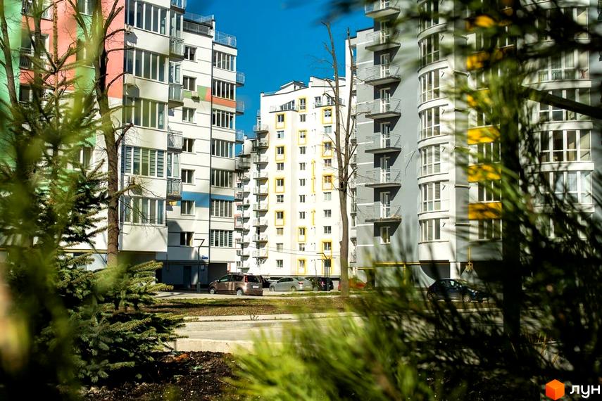 Житловий комплекс Паркове містечко з різнокольоровими фасадами та балконами на тлі блакитного неба. Навколо новобудов ростуть дерева та зелені насадження.
