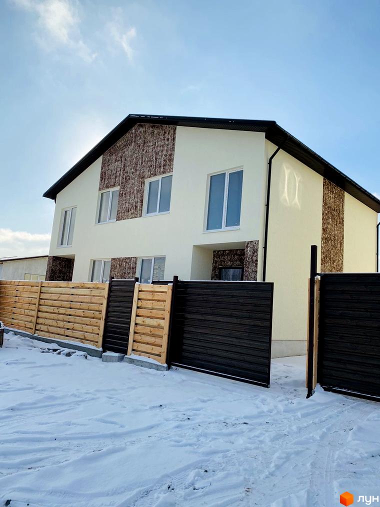 Зовнішній вигляд котеджного містечка КМ Сонячний будинок з дерев'яним та темним парканом на тлі блакитного неба та снігової місцевості.