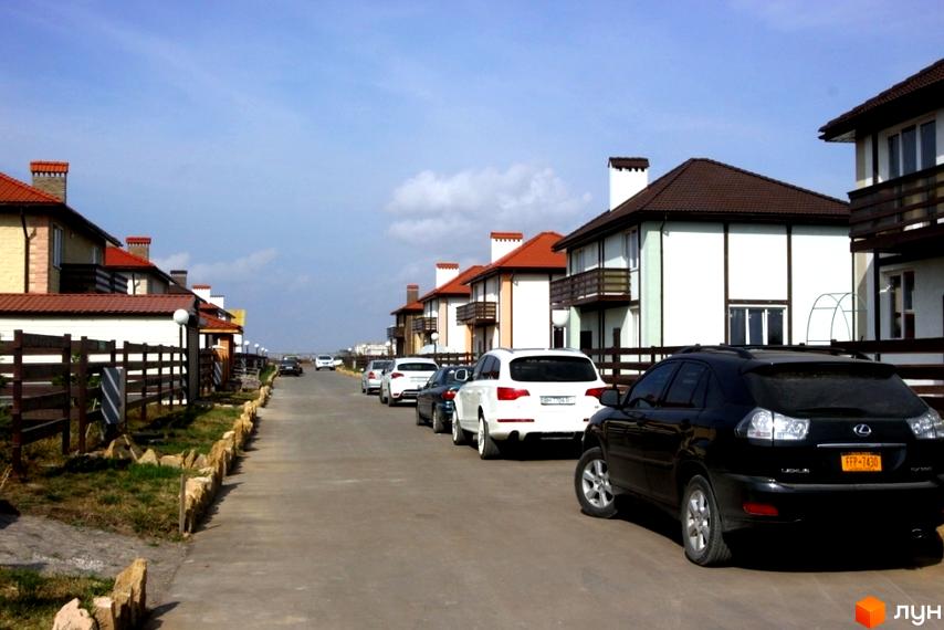 Зображення житлового комплексу Fresh Town. Двоповерхові будинки з червоними дахами та білими стінами. На вулиці припарковані автомобілі.