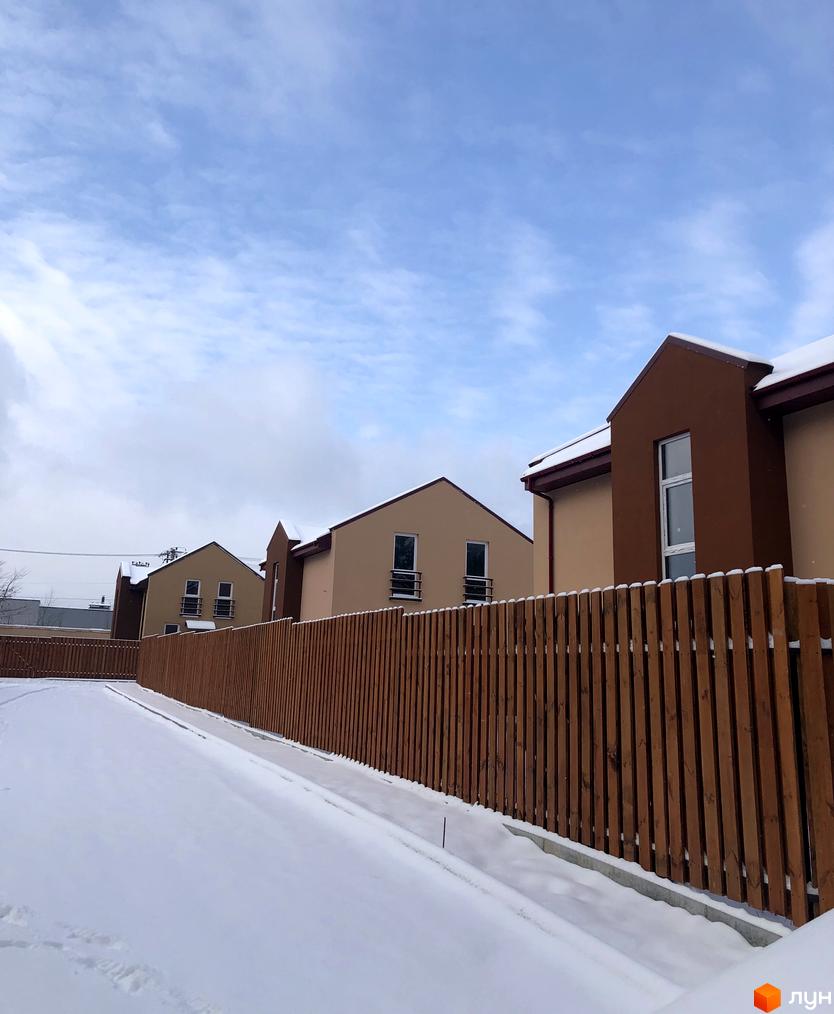 Котеджне містечко Sunny Village: будинки з бежевими та коричневими фасадами, вкриті снігом. Перед ними дерев'яний паркан та засніжена територія.