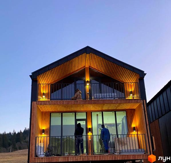 Котеджне містечко Phoenix Relax Park: двоповерховий будинок з дерев'яним фасадом, великими вікнами та балконами. Навколо ліс та відкрита місцевість.