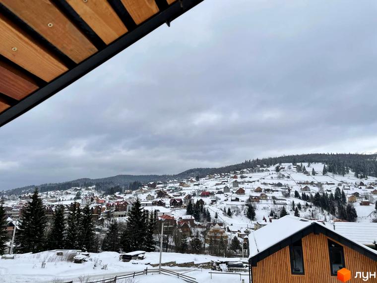 Зимовий краєвид Котеджного містечка Phoenix Relax Park з дерев'яними котеджами під снігом. Навколо сосновий ліс та засніжені пагорби.