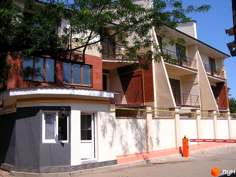 Зовнішній вигляд таунхаусу „Морський“ з червоної цегли з великими вікнами. На передньому плані білий паркан з чорною огорожею.