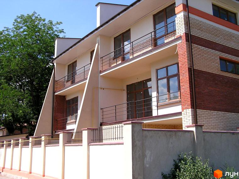 Таунхаус „Морський“: триповерхова будівля з бежевими стінами, цегляними елементами та балконами. Перед будинком – огорожа та зелені насадження.