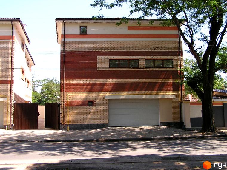 Фасад Таунхаусу „Морський“ з цегляною кладкою світлих та червоних відтінків, гаражними воротами. Перед будинком асфальтований під'їзд та зелене дерево.