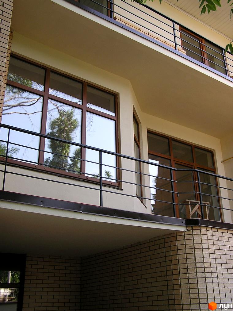 Фасад Таунхаусу „Морський“ з бежевими стінами, великими вікнами у коричневих рамах та чорними балконами. На вікнах видно відображення дерев.