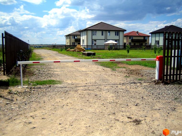 Будинки в Котеджному містечку Fresh Town з білими стінами та коричневими дахами. Перед будинками розташована зелена галявина та дорога з шлагбаумом.