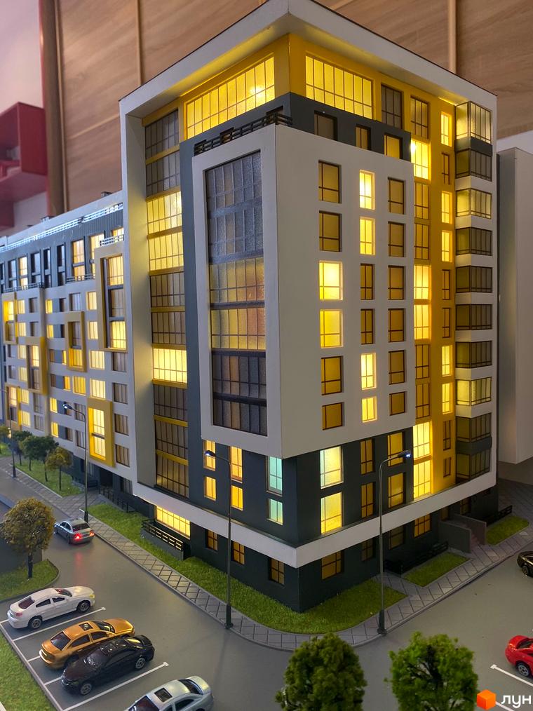 Макет багатоповерхового будинку ЖК «Квартал Енергія» з підсвіченими вікнами. На прибудинковій території розташовані дерева, парковка з автомобілями.