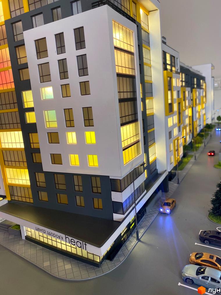 Макет багатоповерхового будинку ЖК з великими вікнами та підсвіткою. На прибудинковій території розташовані паркувальні місця та дорога.