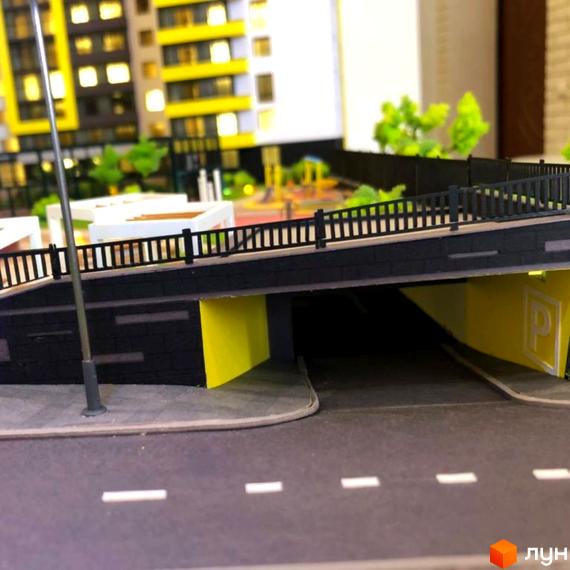 Макет житлового комплексу Квартал Енергія з мостом та підземним паркінгом. На задньому плані видно будівлі з жовтими балконами та дитячий майданчик.