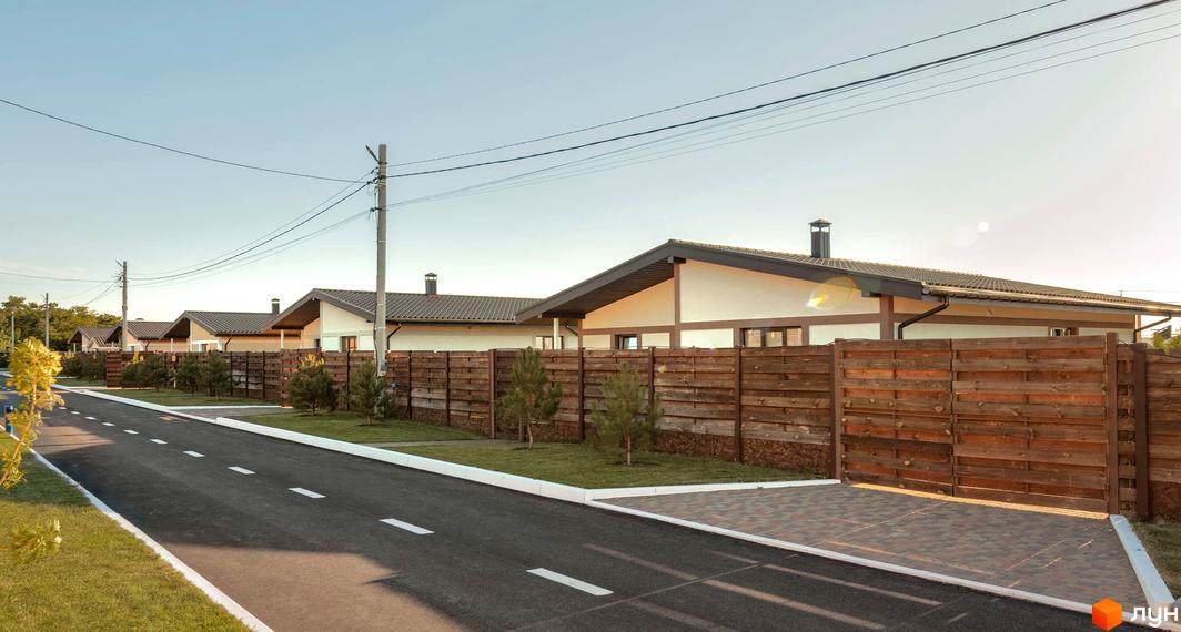 Котеджне містечко Графський: ряд одноповерхових будинків з темними дахами, світлими фасадами, дерев'яними огорожами та асфальтованою дорогою.