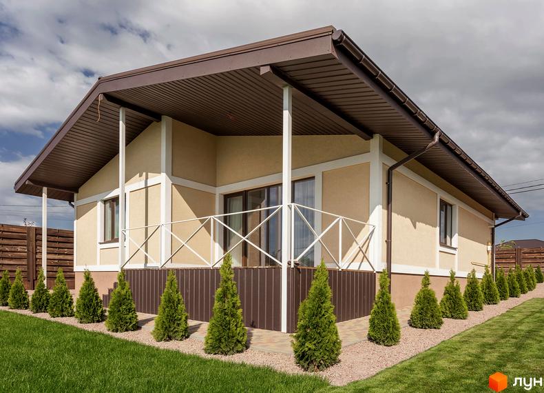 Будинок у Котеджному містечку Графський з бежевими стінами, коричневим дахом та ганком. Прибудинкова територія має зелений газон та ряд туй.