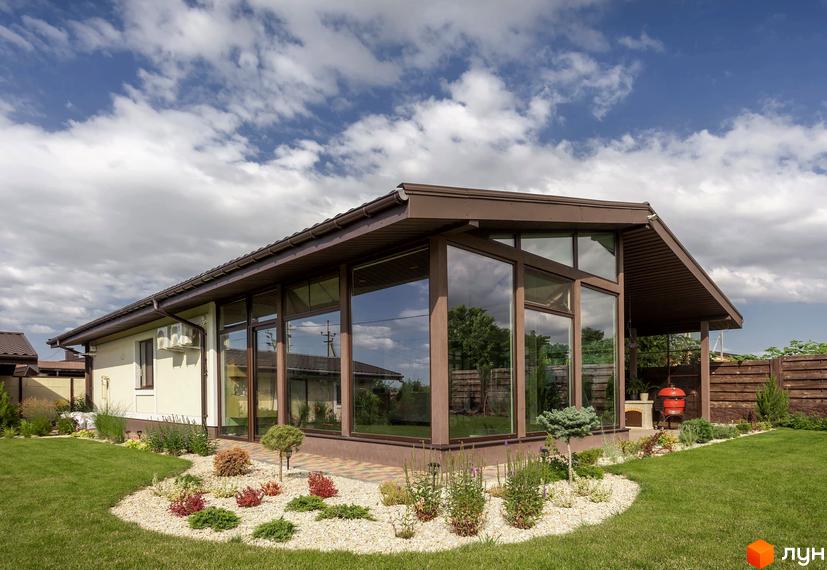 Будинок Котеджного містечка Графський з великими вікнами та коричневим дахом. Навколо доглянутий газон та ландшафтний дизайн з гравієм.