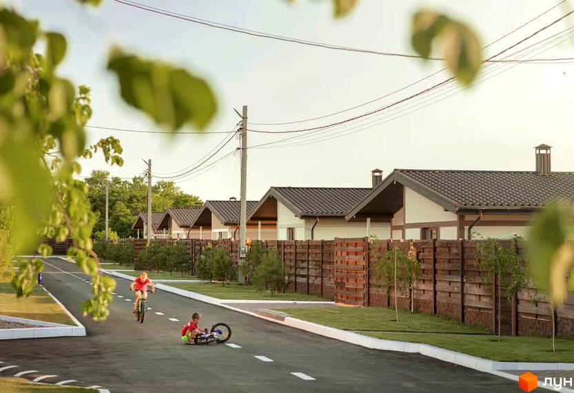 Будинки Котеджного містечка Графський з темними дахами та світлими фасадами, перед якими дерев'яний паркан. На дорозі граються діти.