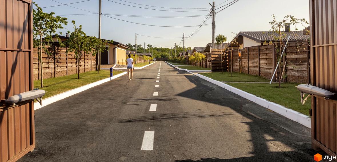 Вигляд на дорогу в Котеджному містечку Графський. Навколо будинки з дерев'яними парканами та зелені насадження.