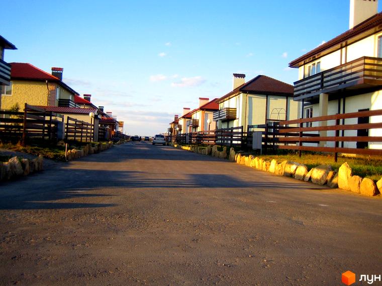 Вулиця в Котеджному містечку Fresh Town з двоповерховими будинками з балконами та коричневими дахами. Дорога з асфальтовим покриттям, з боків якої розташовані кам'яні бордюри.