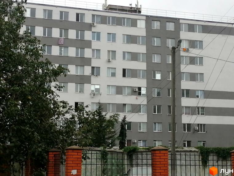 Житловий комплекс Будинок на Боровського: багатоповерховий будинок з сіро-білим фасадом, частково прихований деревами та парканом.