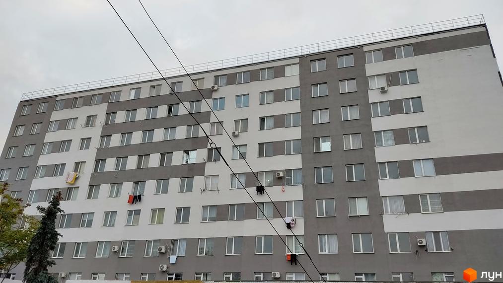 Будинок на Боровського - це новий житловий комплекс з сірими та білими фасадами та великою кількістю вікон. На балконах сушиться білизна.