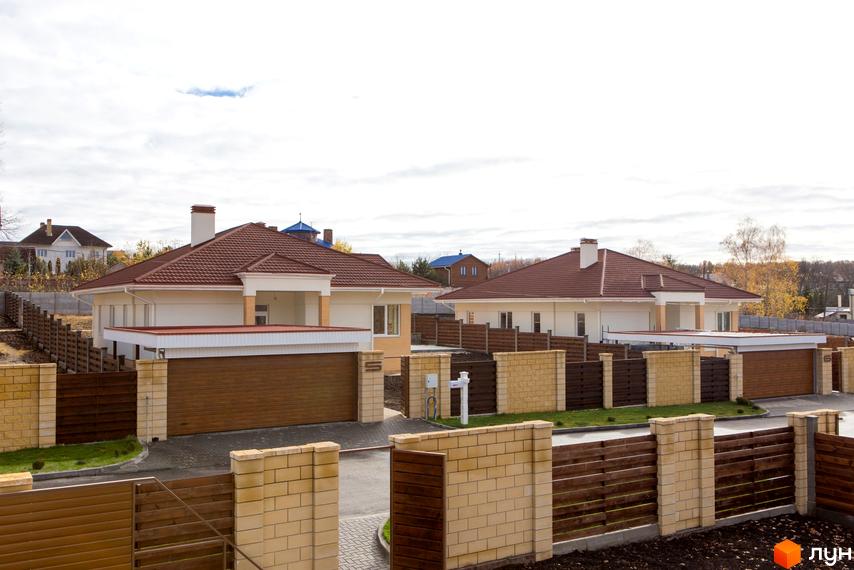 Фото Котеджного містечка Country House з будинками з коричневими дахами та гаражами. Навколо будинків зелені насадження та цегляний паркан.