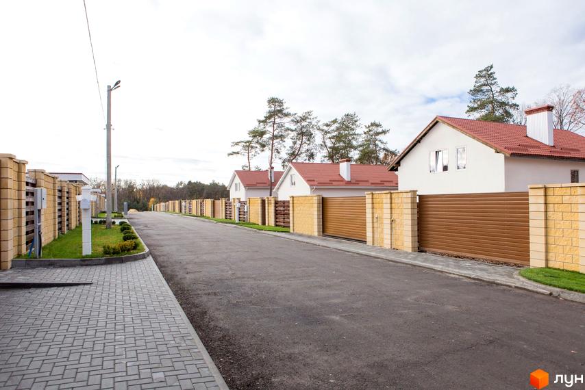 Котеджне містечко Country House: білі будинки з червоними дахами, розташовані вздовж дороги з бруківкою та огорожами з цегли і коричневих панелей.