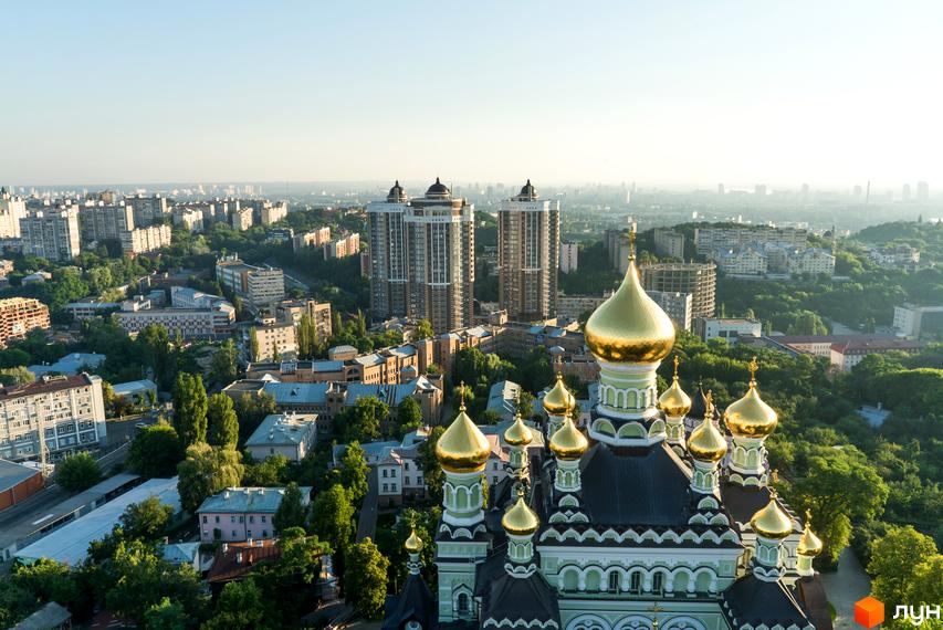 Вид на Житловий комплекс Покровський посад: високі будівлі з темними фасадами та світлими елементами. Навколо комплексу розташовані інші будинки, церква та багато зелені.