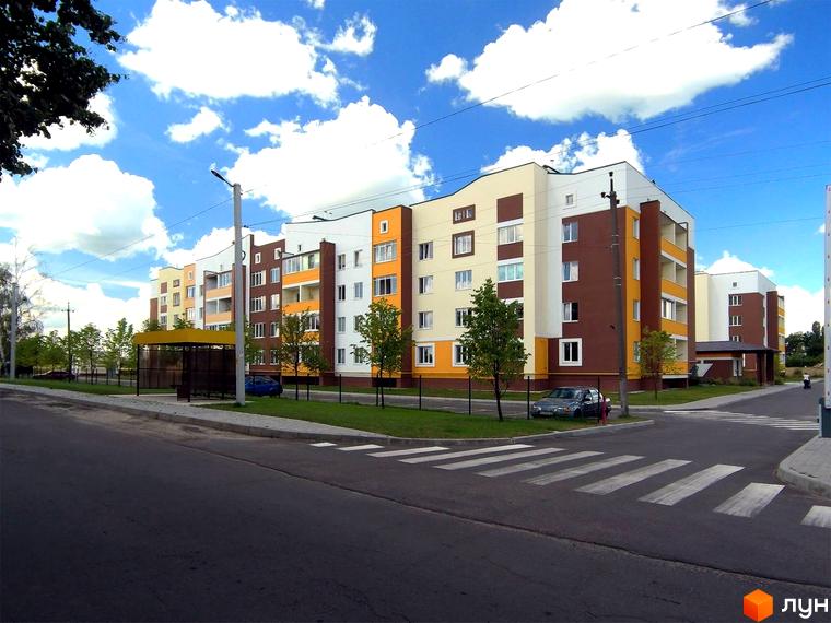 Житловий комплекс Саме Той: багатоповерховий будинок з білими, коричневими та помаранчевими фасадами. Поруч дорога, пішохідний перехід та зупинка.